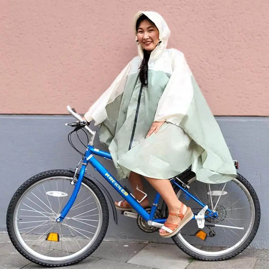 Frau auf dem Fahrrad mit Regencape und Kapuze im Sommer, lächelnd. Der Regenponcho ist hellgrün